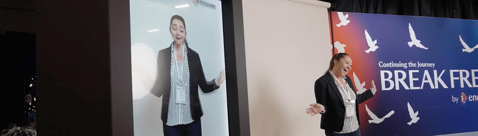 A woman stands on stage at Break Free: IMEX America 2023 | Encore®, her image projected on a large screen. The backdrop reads BREAK FREE with white flying birds and a striking red and blue gradient design.